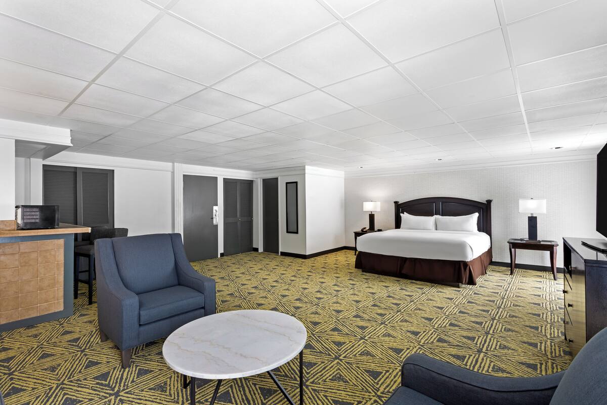 A hotel room with a bed, a desk, a chair, a round table, and a patterned carpet.