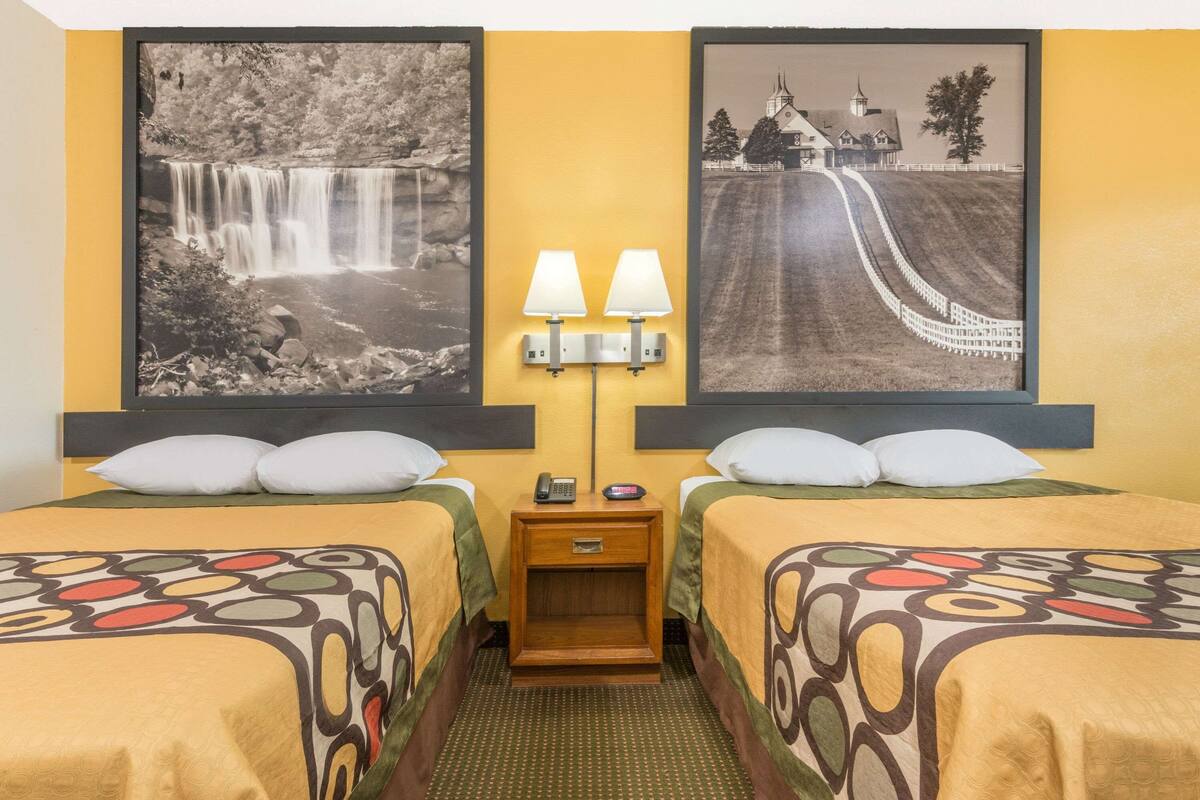 Ein Hotelzimmer mit zwei Betten, einem Nachttisch mit Lampen und zwei gerahmten Bildern an der Wand.
