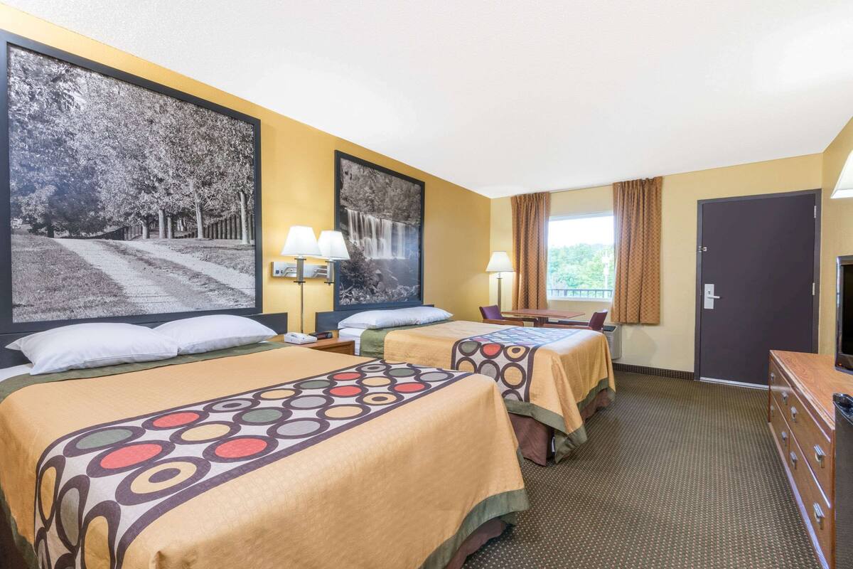 Ein Hotelzimmer mit zwei Betten, einem großen Fenster mit Vorhängen, einem Schreibtisch mit Stuhl und einer Kommode.