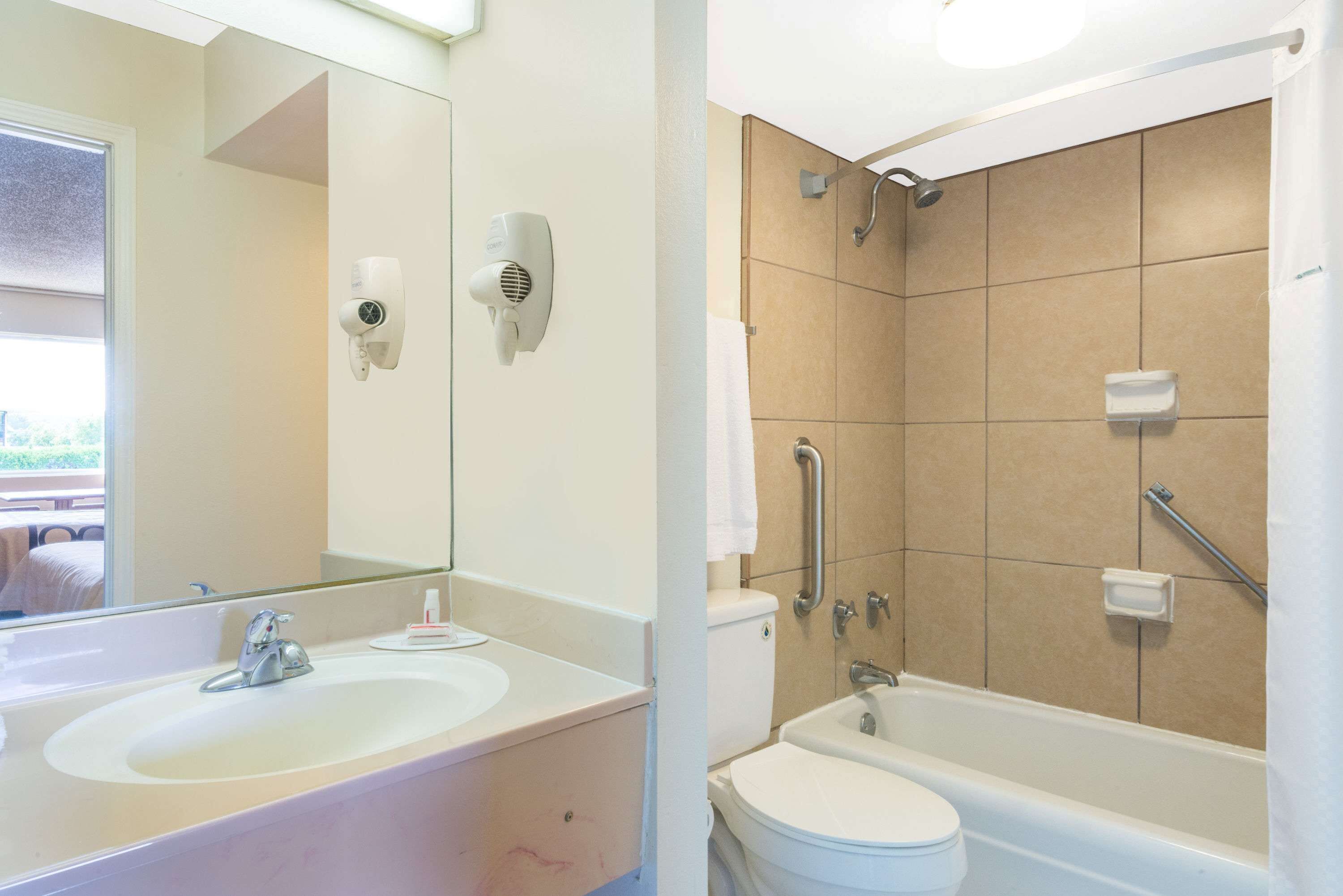 A bathroom with a sink, mirror, hair dryer, toilet, and bathtub.