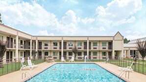 A hotel with a swimming pool, multiple balconies, and a fenced outdoor area with lounge chairs.