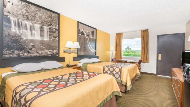 A hotel room with two beds, a desk, a chair, a TV, and a window with a view of greenery.