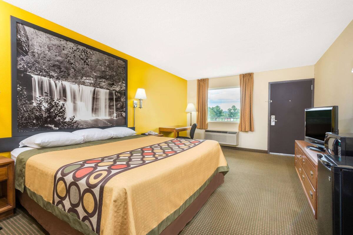 Ein Hotelzimmer mit einem großen Bett, einem Schreibtisch, einem Fernseher und einem Fenster mit Vorhängen.