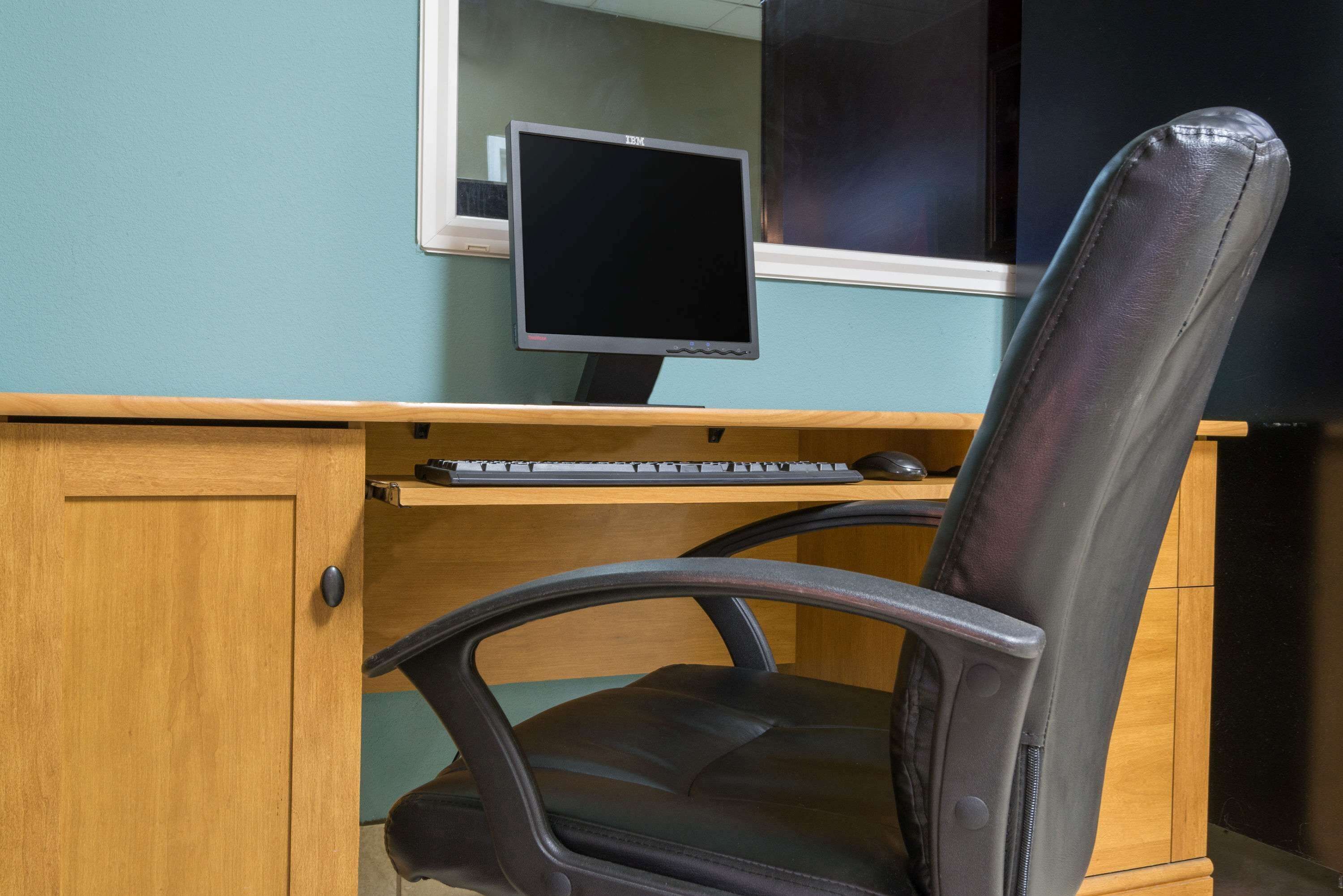 A wooden desk with a computer monitor, keyboard, and a black office chair.