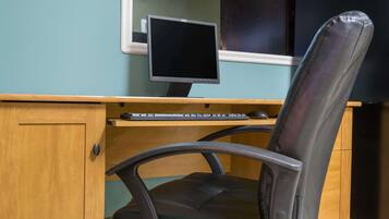 A wooden desk with a computer monitor, keyboard, and a black office chair.
