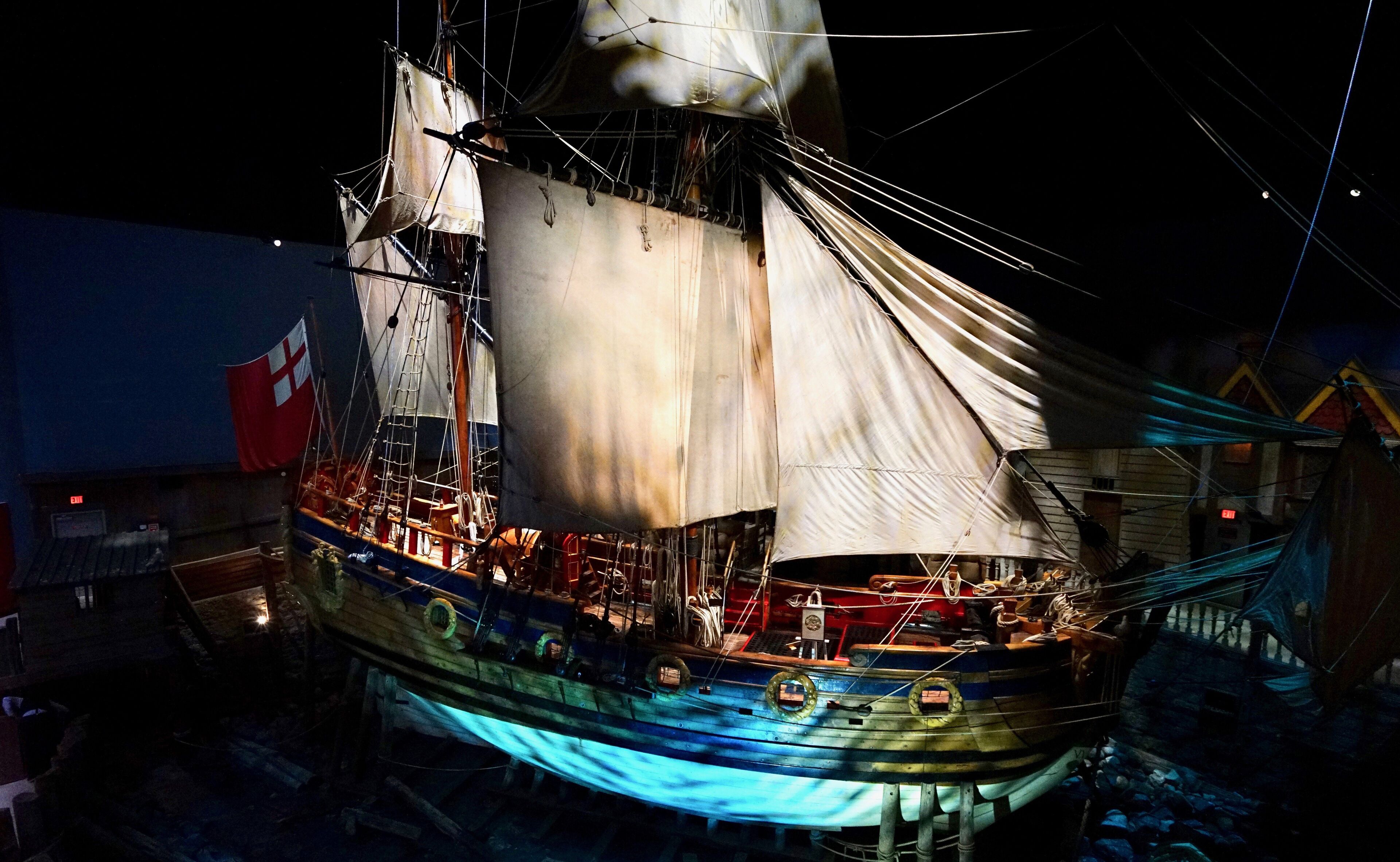 A large ship with multiple masts and sails, docked at a port.
