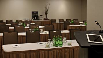 A conference room with multiple tables, chairs, and a long table with green bottles and glasses.