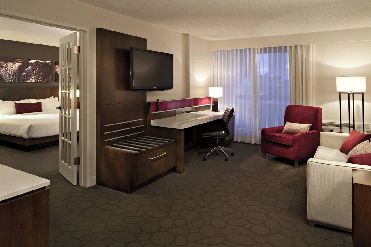 Quarto de hotel com cama, escrivaninha, cadeira e televisão.