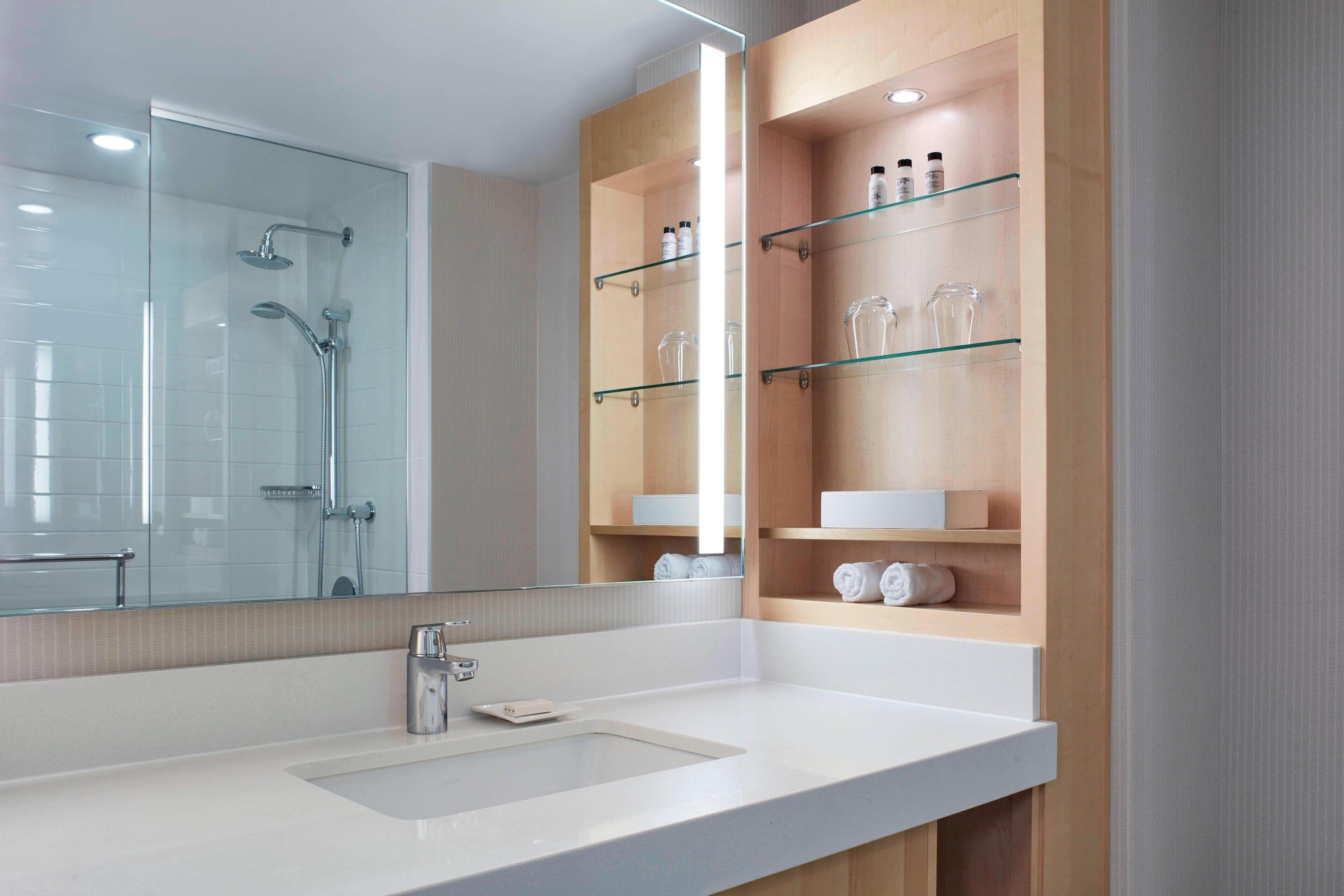 Un baño moderno con cabina de ducha de vidrio, un lavabo blanco y estantes empotrados con artículos de aseo.