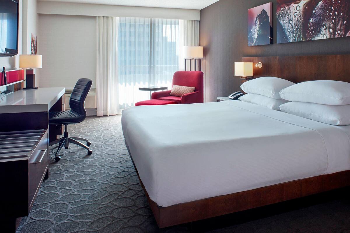 Quarto de hotel com uma cama grande, uma mesa com cadeira, uma mesinha e duas luminárias.