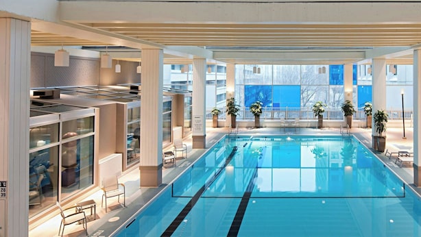 Una amplia piscina interior con zona poco profunda, rodeada de sillones de descanso y plantas en macetas.