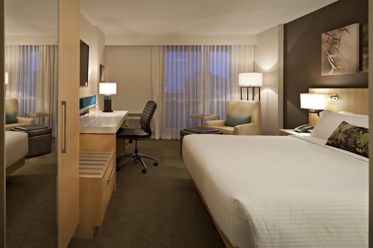 Quarto de hotel com cama, escrivaninha, cadeira e uma pequena mesa.