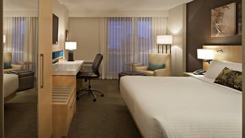 A hotel room with a bed, desk, chair, and a small table.