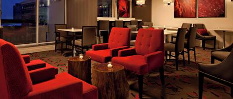 A hotel lobby with red upholstered chairs, wooden side tables, and artwork on the walls.