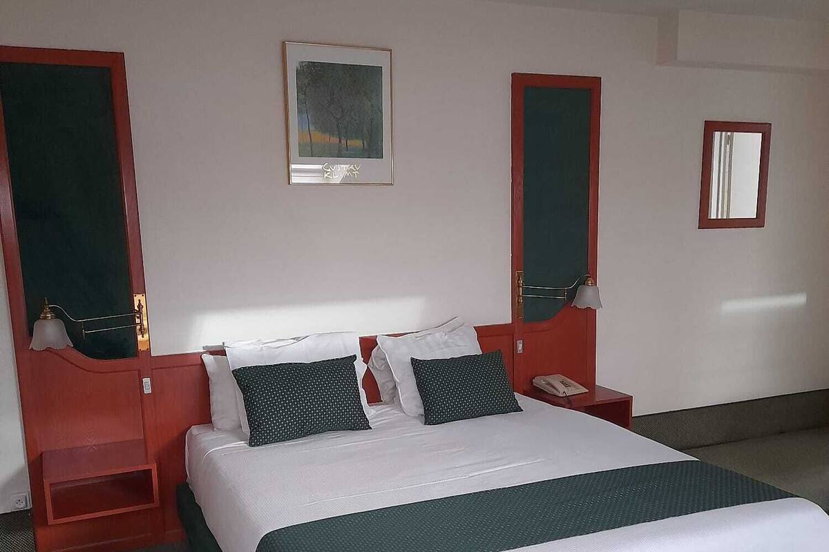 Habitación de hotel con una cama grande, dos mesitas de noche, un escritorio, una silla, un espejo y un cuadro en la pared.