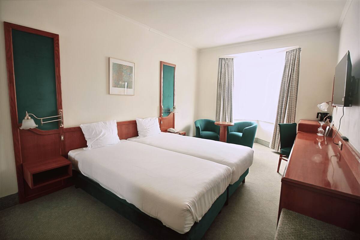 Habitación de hotel con dos camas, un escritorio, una silla, un televisor y una ventana con cortinas.
