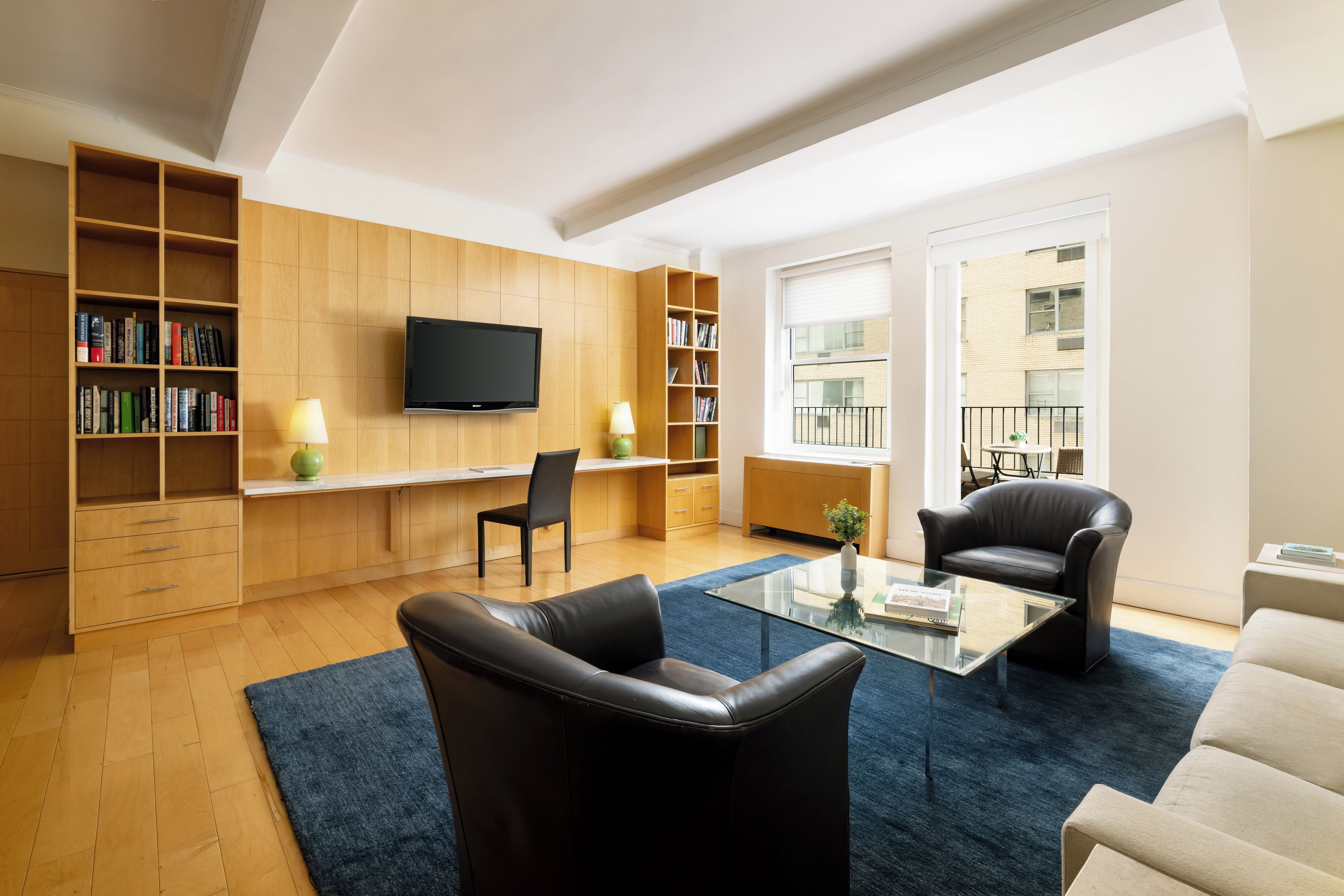 A modern living room with a flat-screen TV, bookshelves, a coffee table, and leather chairs.