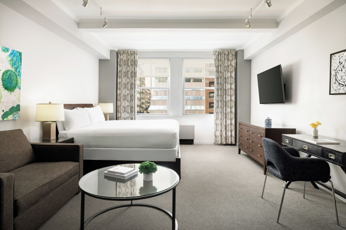 A hotel room with a bed, a desk, a chair, a coffee table, and a TV.