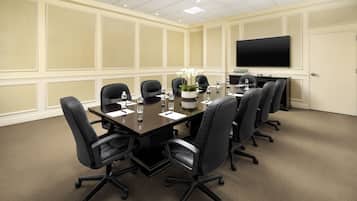A conference room with a large table, black chairs, a flat-screen TV, and a potted plant.