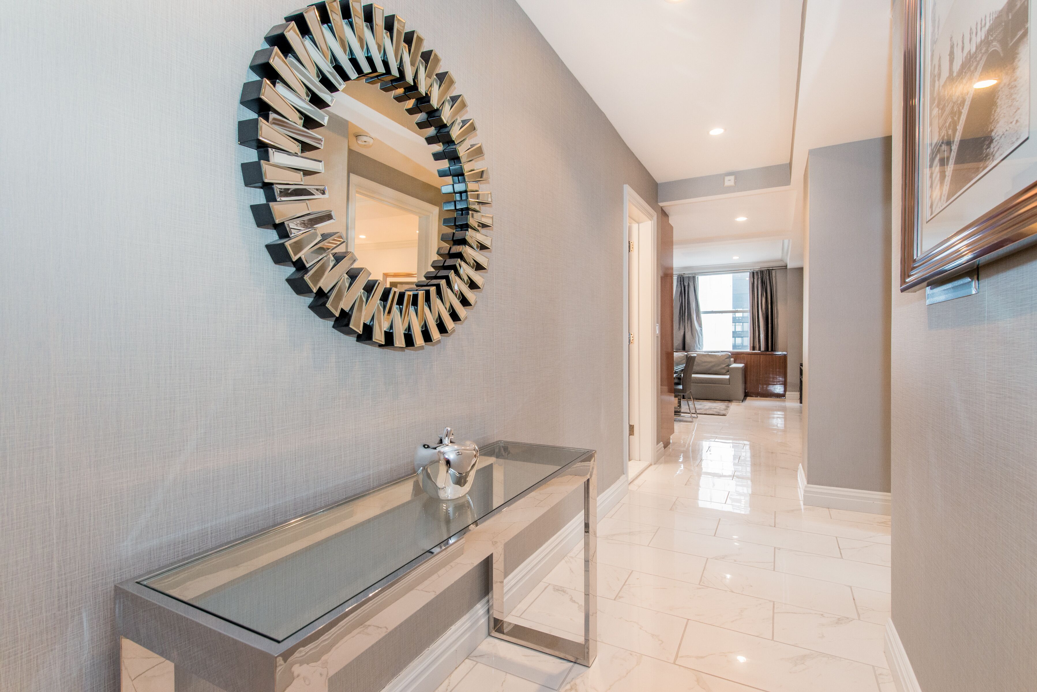 A modern bathroom with a glass vanity, a unique circular mirror, and a hallway leading to a dining area.