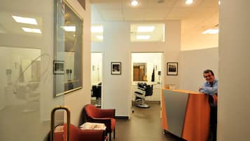 L’intérieur d’un salon de coiffure, avec un comptoir d’accueil, deux fauteuils d’attente et un miroir.