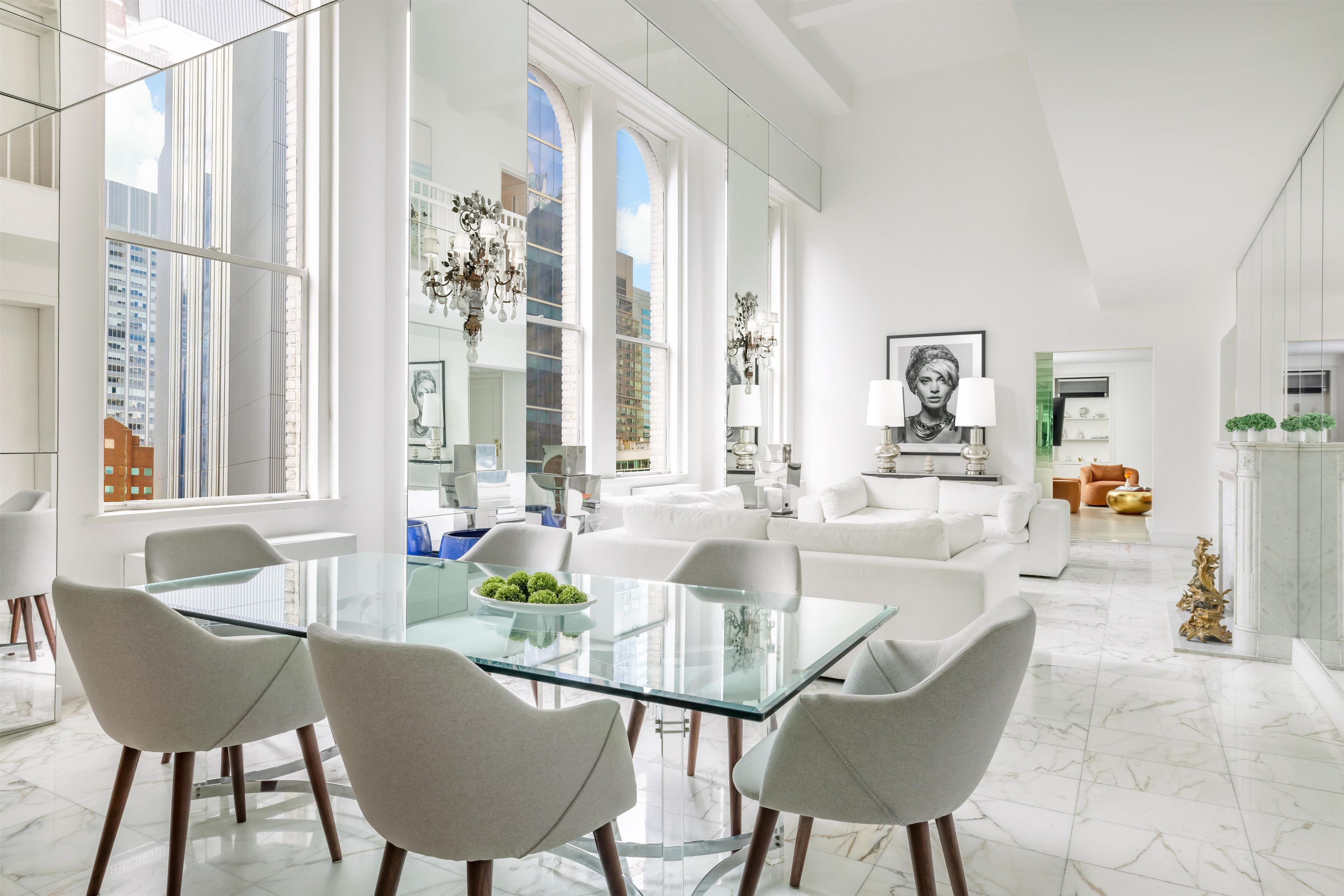 A spacious living area with a glass dining table, modern furniture, and large windows offering views of the city.
