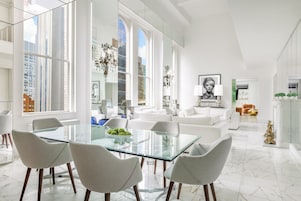 A spacious living area with a glass dining table, modern furniture, and large windows offering views of the city.