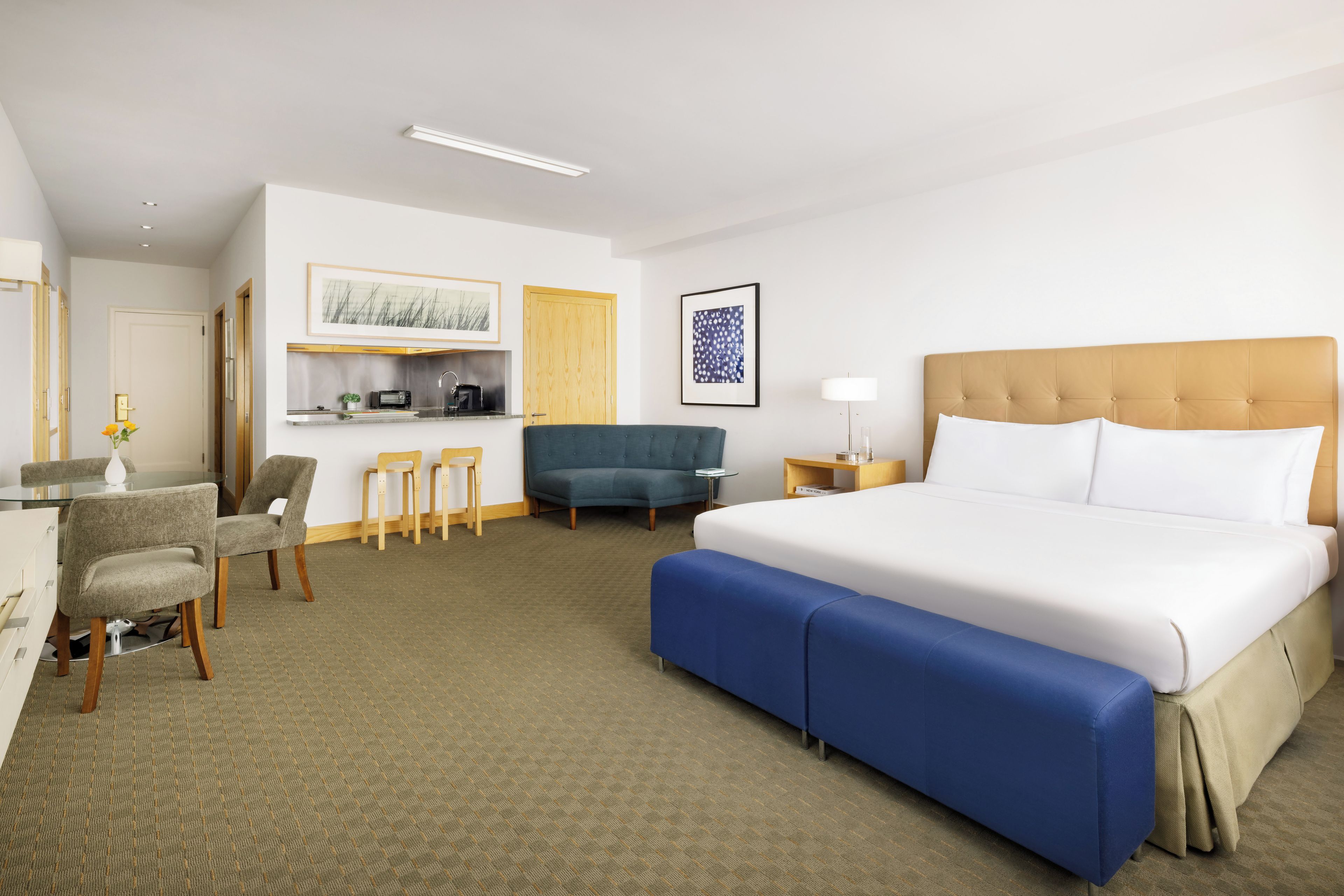 Habitación de hotel con una cama grande, un escritorio con silla, un sofá, una kitchenette pequeña y un área de comedor.
