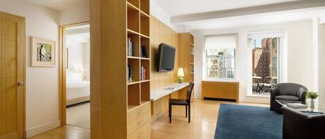A modern living room with a wooden bookshelf, a flat-screen TV, a dining area with a table and chairs, and a view of the city through large windows.