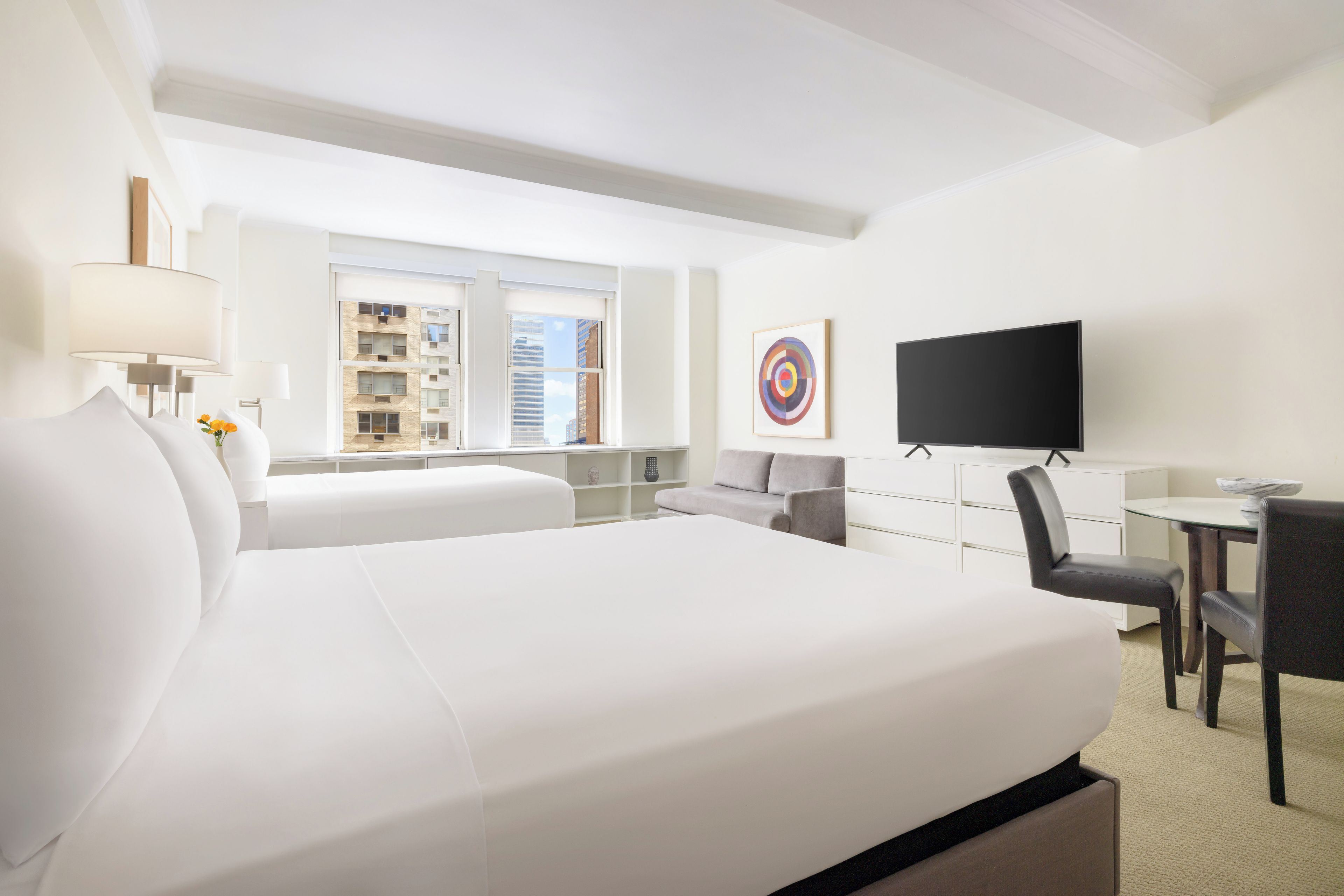 A hotel room with a large bed, a desk, a TV, and a window with a city view.