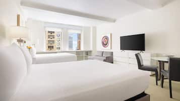 A hotel room with a large bed, a desk, a TV, and a window with a city view.