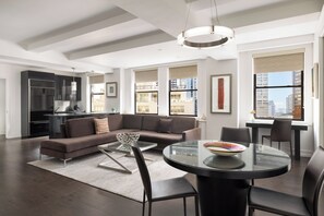A modern living room with a sectional sofa, a glass coffee table, and a dining area with a round table. - The Lombardy Hotel (New York)