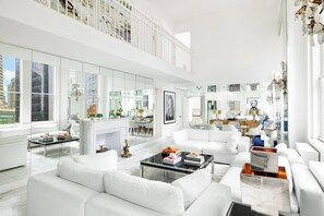 Un salón moderno con muebles blancos, chimenea y ventanas amplias que ofrecen vistas a la ciudad.