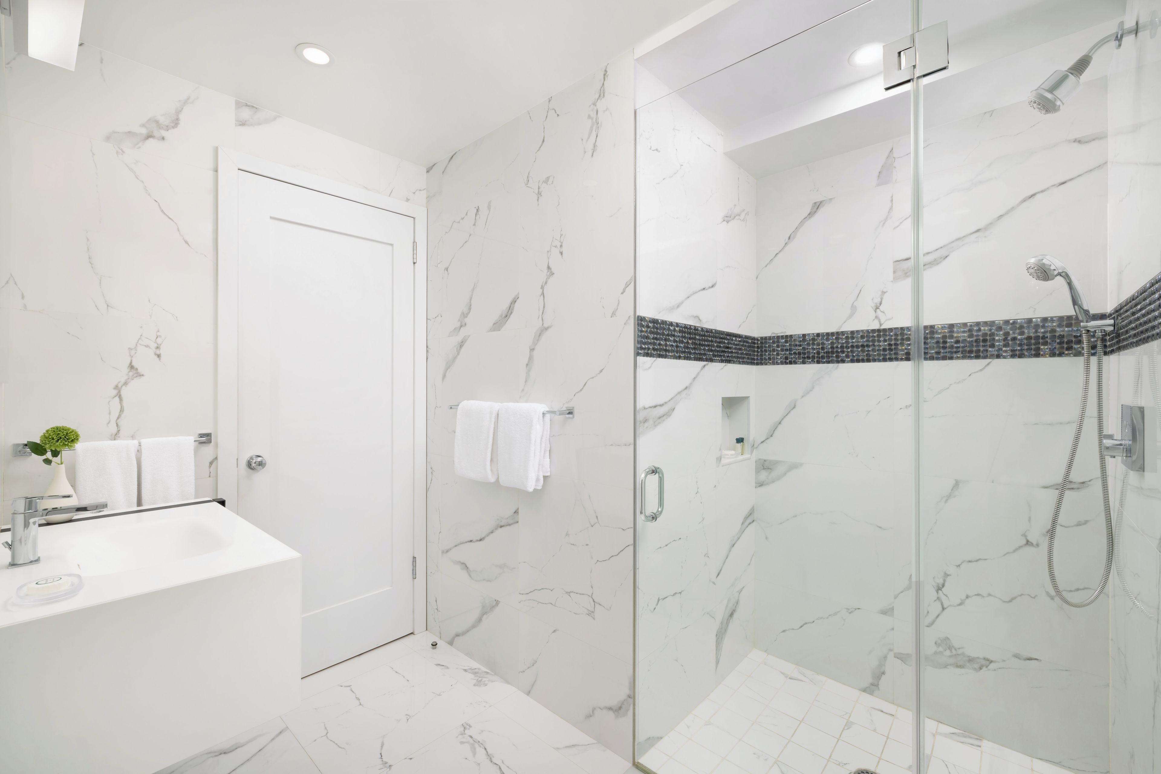 A modern bathroom with a glass shower enclosure, a white marble wall, and a white sink.
