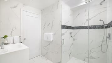 A modern bathroom with a glass shower enclosure, a white marble wall, and a white sink.