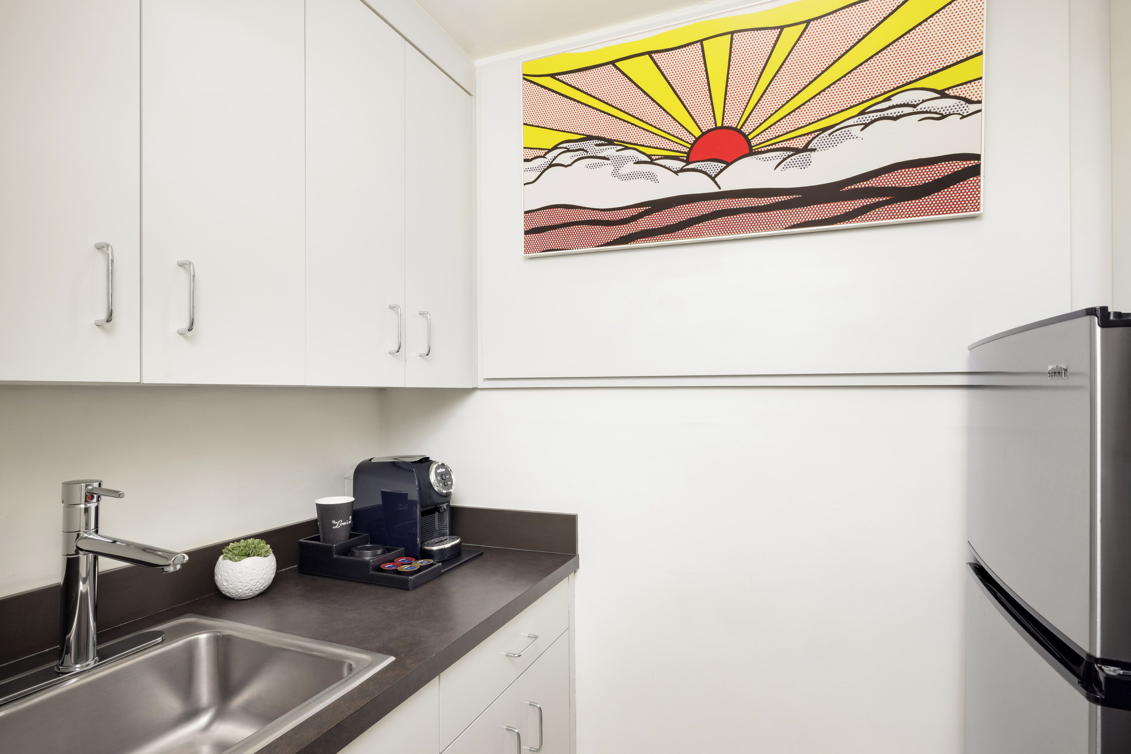 Una cocina con un lavamanos de acero inoxidable, una cafetera y un refrigerador.