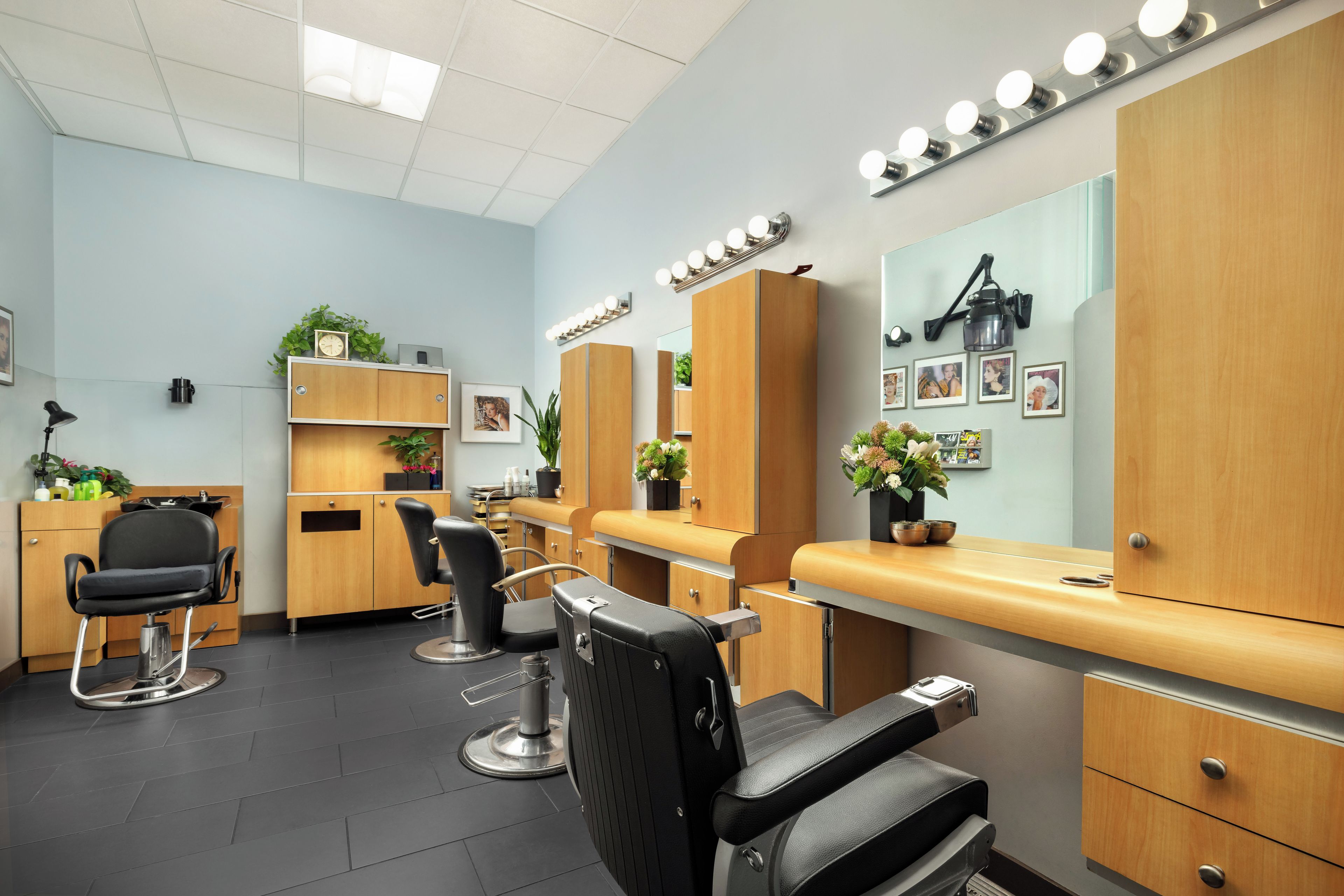 A salon with a reception desk, two chairs, a mirror, and a shelf with plants.