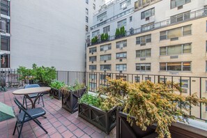 A rooftop terrace with outdoor seating, potted plants, and a view of adjacent buildings. - The Lombardy Hotel (New York)