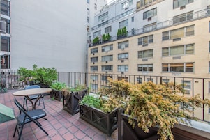 A rooftop terrace with outdoor seating, potted plants, and a view of adjacent buildings.