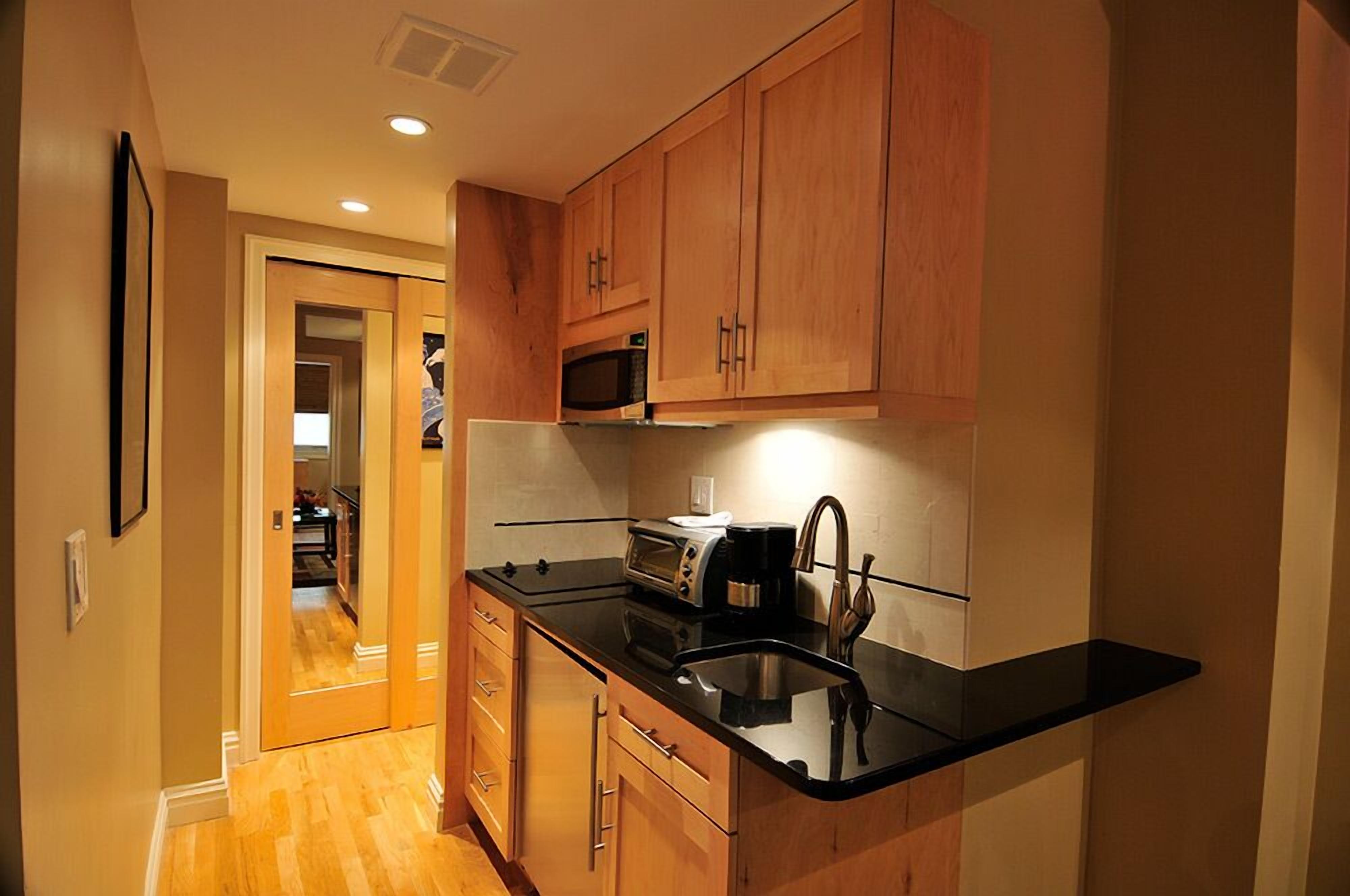 A compact kitchen with wooden cabinets, a black countertop, a built-in microwave, and a toaster.