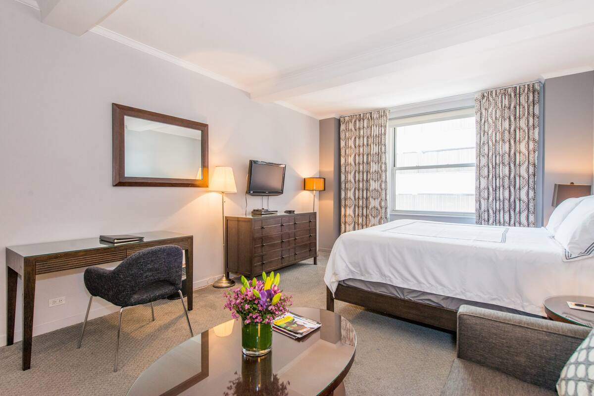 A hotel room with a bed, a desk, a chair, a television, a dresser, and a window with curtains.