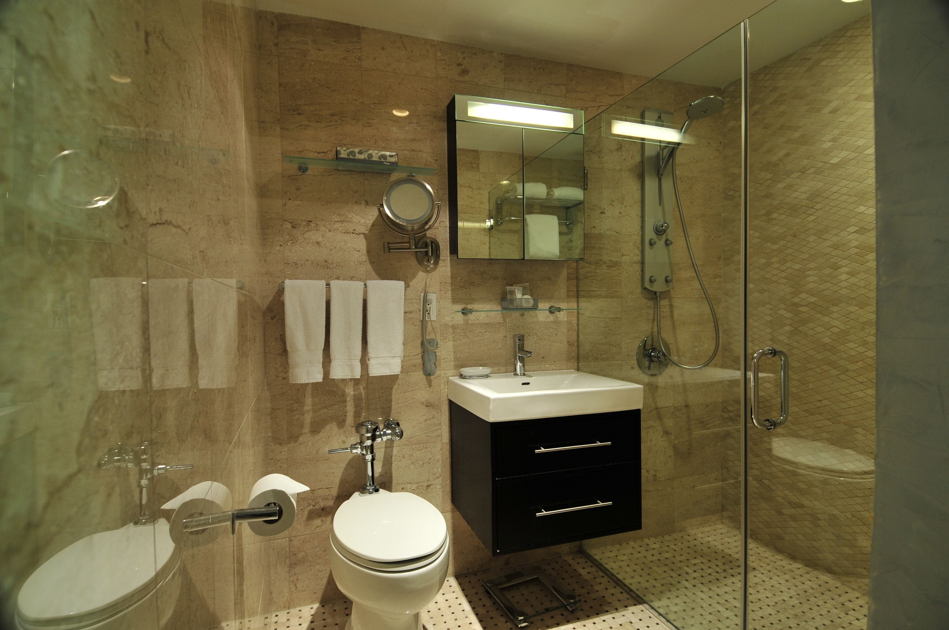A modern bathroom with a glass shower enclosure, a white toilet, a sink with a black cabinet, and a mirror above the sink.