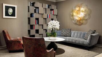 A modern living room with a grey sofa, floral armchairs, a round coffee table, a bookshelf, and a decorative wall piece.