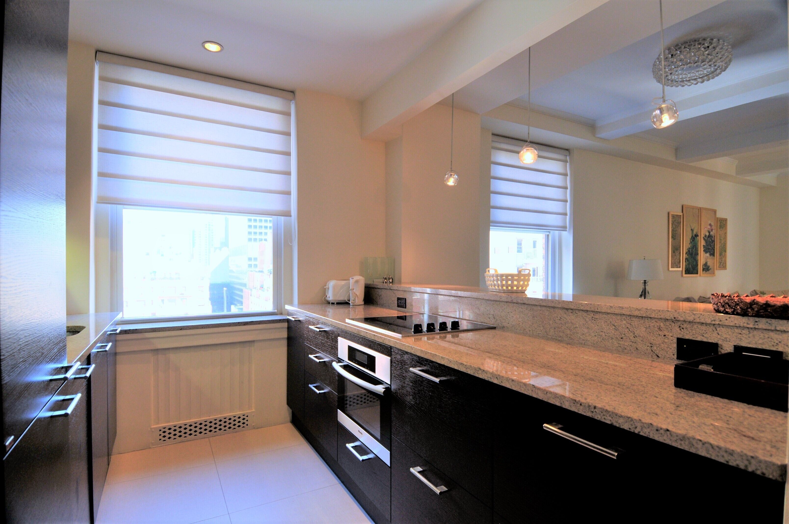 A modern kitchen with a large island, built-in oven, and a window with blinds.
