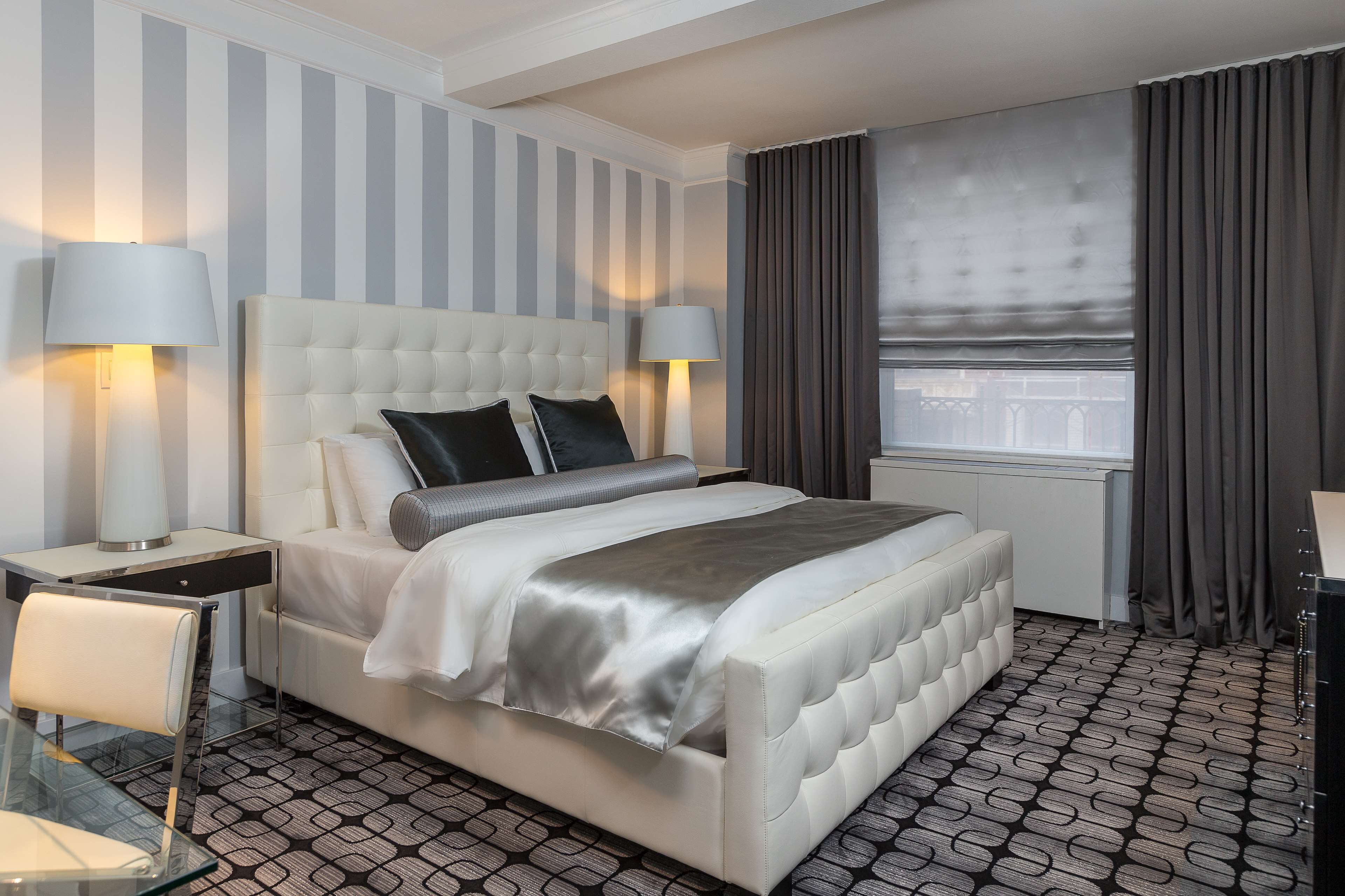 A hotel room with a large bed, two bedside tables with lamps, a glass table, and a patterned floor.