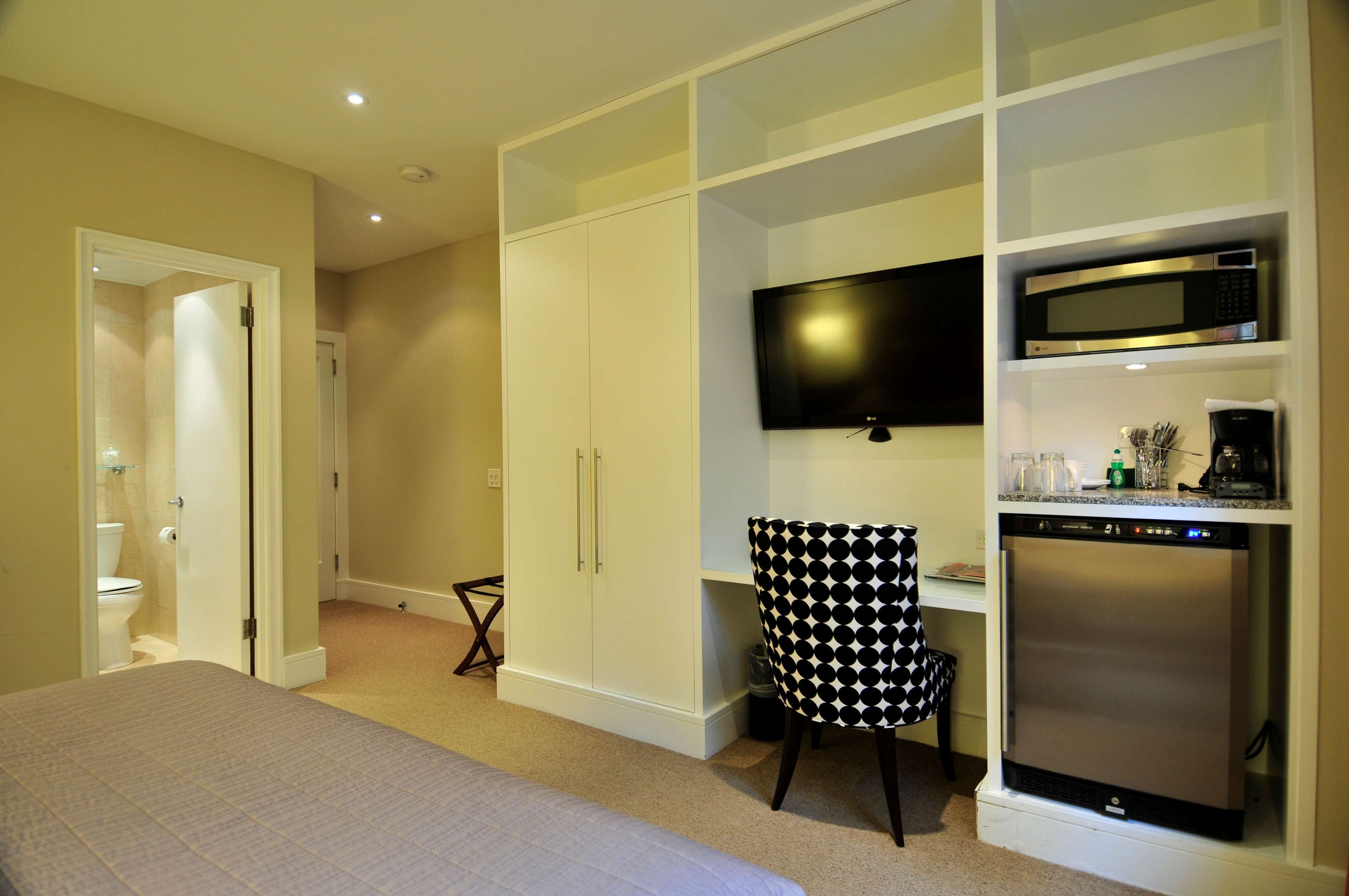 Un dormitorio con cama, escritorio con silla, televisor, microondas y refrigerador.