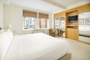 A hotel room with a large bed, a TV, a wardrobe, and a window with a view of buildings.