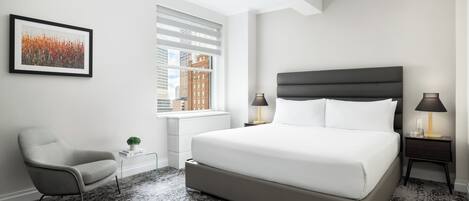 A modern hotel room with a large bed, a chair, a bedside table with a lamp, and a window with a city view.