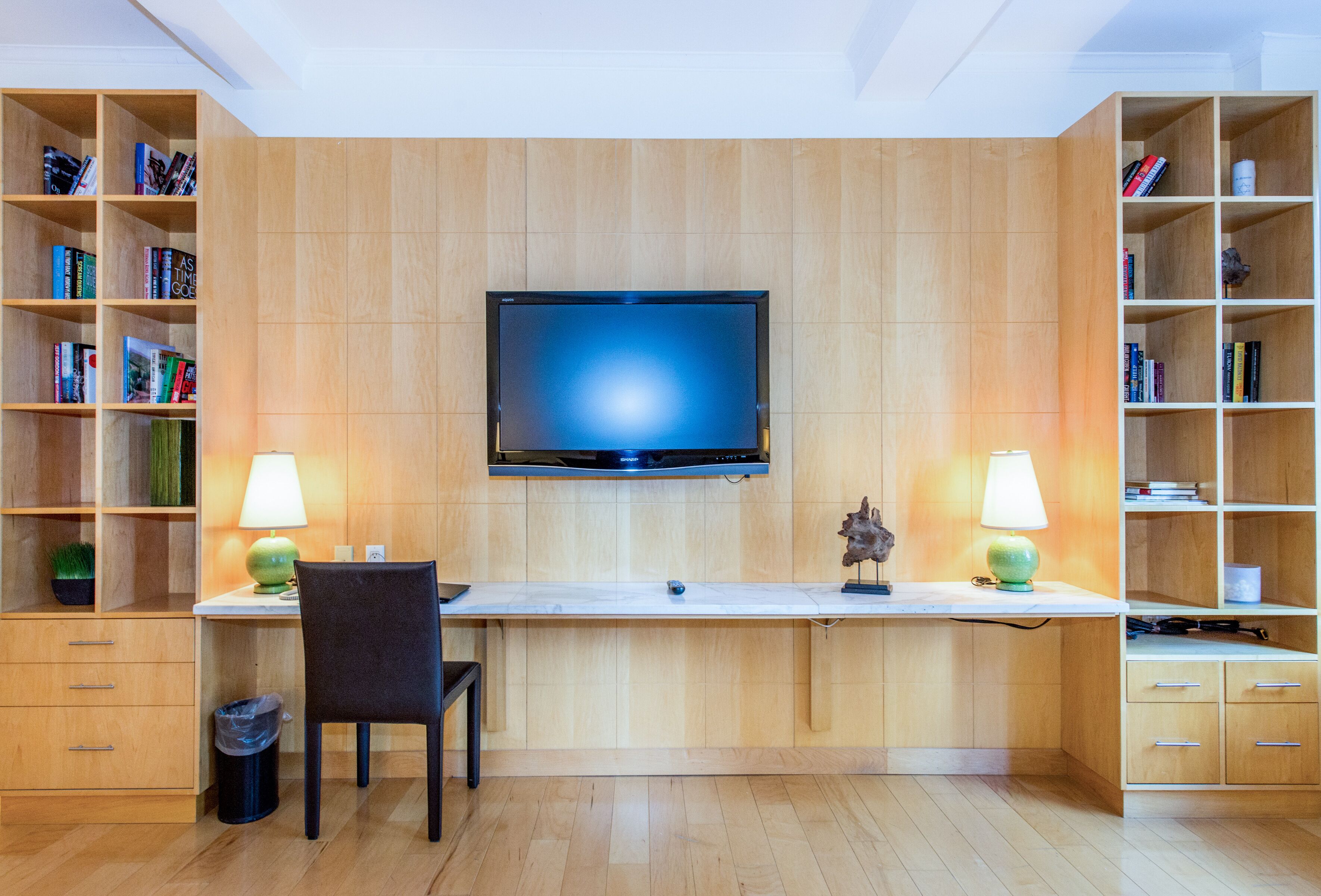 A modern room with a flat-screen TV mounted on the wall, a desk with a chair, and two bookshelves filled with books.