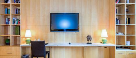 A modern room with a flat-screen TV mounted on the wall, a desk with a chair, and two bookshelves filled with books.